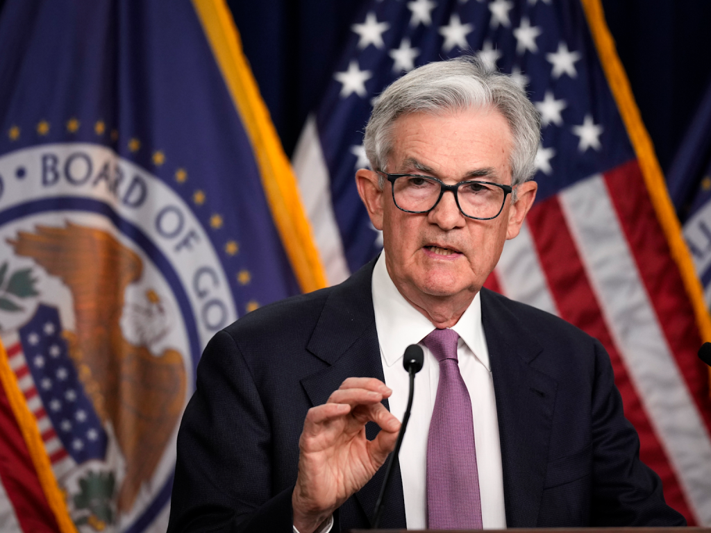 Federal Reserve Chairman Jerome Powell addresses monetary policy with U.S. flags and Federal Reserve emblem in the background